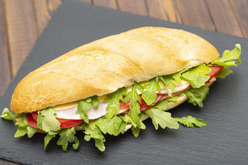 Baguette sandwich with ham, tomatoes, cheese and arugula lettuce. Delicious Breakfast or snack. Close up