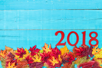 Year 2018 in bold red hanging on antique rustic teal blue wood background with colorful autumn leaves border