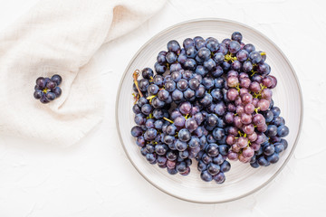 Berries of ripe blue grapes on a plate on a table. Harvesting in autumn. Top view