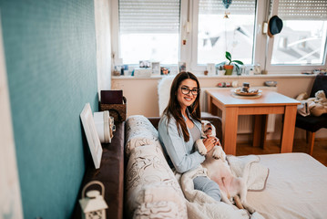 Portrait of cute young woman playing with puppy at home.