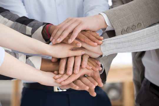 Close up of multiracial group of millennial business people or students standing stacking theirs hands palm together. Gesture sign of support unity and togetherness, starting common business concept