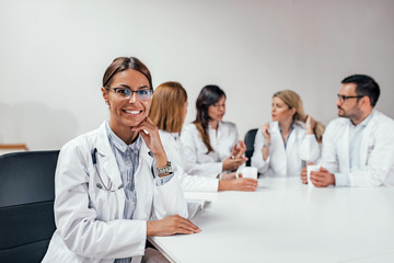 Fototapeta premium Portrait of female doctor sitting at the table having a break, colleagues in the background.