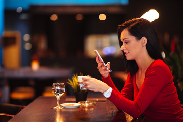 Beautiful young woman suing smartphone and drinking coffee in a cafe