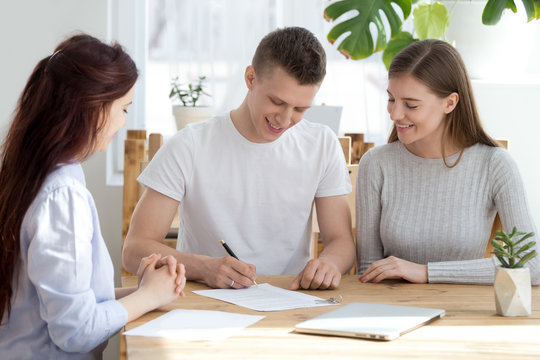Three young millennial people sitting at the desk in office agency. Married family couple happy smiling sign a contract paper document. Relocate move a new home, buying real estate property concept