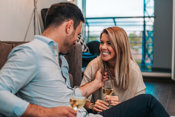 Laughing couple enjoying white wine while sitting on the floor.