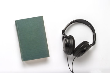 Book with a blue cover and black headphones on a white background. Concept of audiobooks and distance learning. Flat lay, top view