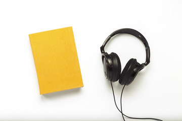 Book with a yellow cover with text English and black headphones on a white background. Concept of...