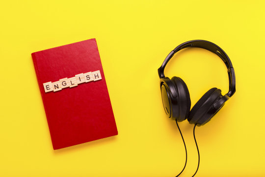 Book with a red cover with text English and black headphones on a yellow background. Concept of audio books, self-education and learning English independently. Flat lay, top view