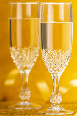 Closeup glasses of Champagne and yellow ribbon on golden background