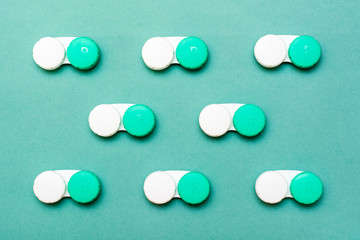 Lens containers lie in neat rows on a green background. Top view