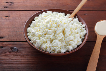 Cottage cheese. Cottage cheese and cream on wooden boards. Soft cheese in earthenware dish. Dairy products with wooden spoon. Sour cream in spoon. Copy space