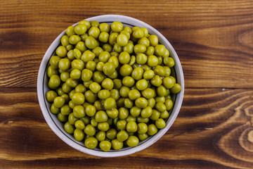 Bowl with canned green peas  on wooden table. Top view
