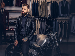 Obraz na płótnie Canvas Brutal male dressed in black jacket leaning on a retro sports motorbike at the men's clothing store.
