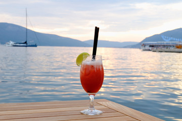 Cocktail glass with lemon on wood table with seascape and skyline in the evening with sunset tone style Sea wave background Background of stunning turquoise sea Travel concep