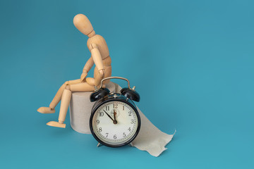 Wooden figure sit on a roll of toilet paper near alarm clock. Concept of the problem with digestion.