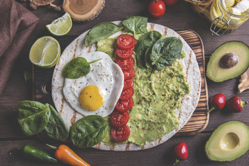 tortilla with guacamole avocado, fried egg and tomato, spinach leaves. vegetarian dish