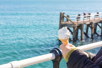 Womans Hands Holding an Ice Cream in a Cone With a Metal Rail and the Sea Beyond