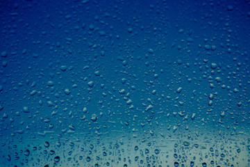 raindrops flow down the window of a house on the background of a blue sky. Close-up