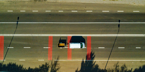 a car with a trailer drives along a highway with red marked lines. Aerial view