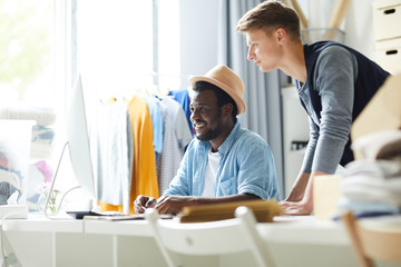 Two young male intercultural designers looking at computer screen while choosing suitable trendy colors for new project