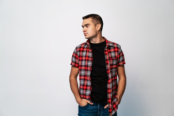 stylish man in a plaid shirt and jeans stands with hands in pockets on a white background. Handsome face profile of man