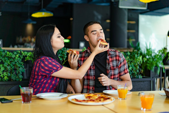 enamored woman gives a guy a piece of pizza in the restaurant on the background of the interior of green plants. Young couple have lunch at a cafe
