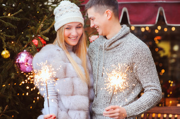 happy loving couple enjoying Christmas or New year Holidays outdoor on city streets decorated for celebration with burning firelights