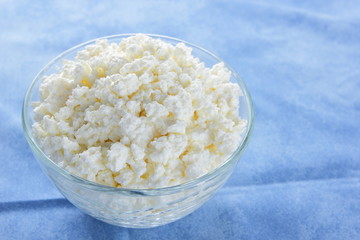 Cottage cheese. Cottage cheese on blue napkin. Soft cheese in glassware. Dairy product for breakfast. Copy space