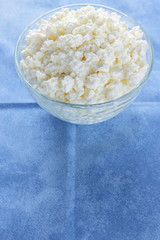 Cottage cheese. Cottage cheese on blue napkin. Soft cheese in glassware. Dairy product for breakfast. Copy space