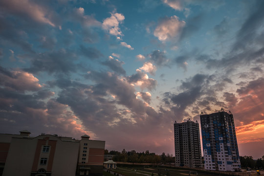 evening fluffy curly rolling clouds of awesome sunset against the background of multi-storey apartment buildings