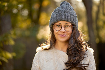 face of a beautiful woman in a cap and glasses on a background of autumn forest