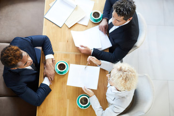 Directly above view of serious employers sitting at table and interviewing job candidate in cafe,...