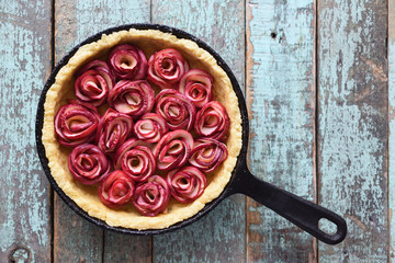 Yummy healthy pie. Apple rose tart in cast iron pan on old blue background