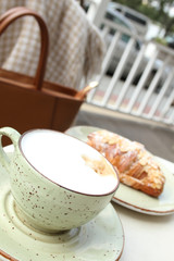 A cup of latte coffee and a croissant in a summer cafe on the table