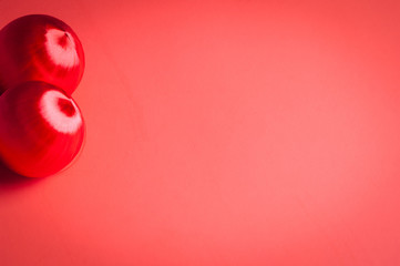 Two red shiny Christmas balls set on the left side of a gently gradient and smooth red paper background in horizontal format.