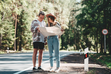 Obraz premium Man and woman traveling together and hold in hands location map and searching directional among trees in forest. Ypung hipster couple hiking on forest road