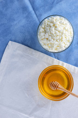 Cottage cheese. Cottage cheese and honey on white blue background. Soft cheese in glassware. Dairy product for breakfast. Copy space