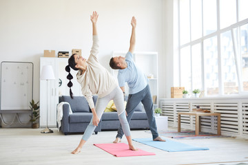 Young sporty couple in activewear raising their left arms while exercising in living-room at home