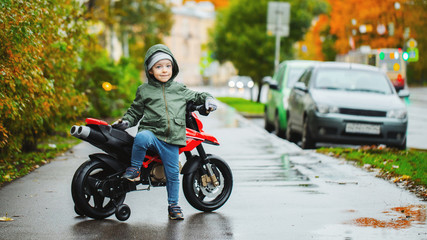 Fototapeta premium A beautiful little boy posing at his children's red motorcycle. The concept of teaching children to motor vehicles from an early age