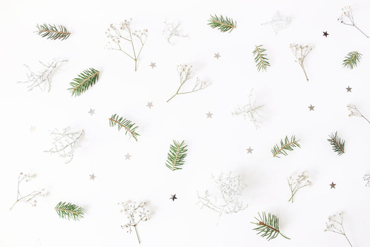 Christmas floral pattern. Winter composition of green spruce tree branches, baby's breath flowers, Calocephalus brownii and silver confetti stars on white table. Festive background. Flat lay, top view