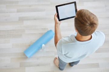 Young man in activewear standing on the floor while searching for workout videos in the net