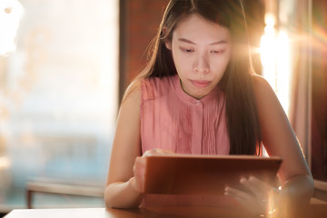 Woman looking on her tablet for social network at coffee cafe in sunset light.