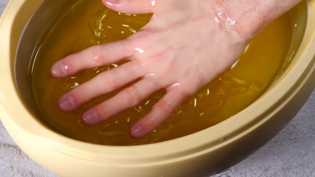 Close up slow motion shot of unrecognizable woman putting hand into paraffin bath taking care of hands skin.