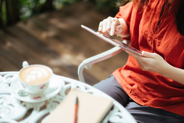 Woman holding tablet computer and coffee cup in coffee shop.