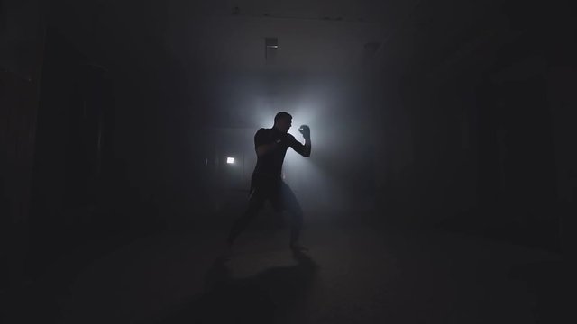 Boxer training in low light gym in slow motion. Sportsman boxing in smoky studio. Silhouette on dark background with copy space