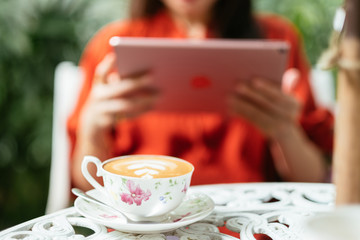 Woman holding tablet computer and coffee cup in coffee shop.