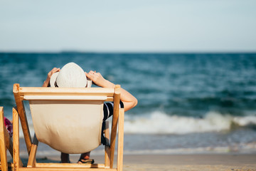 Woman relaxing on deck chair at the tropical beach in sunset light.