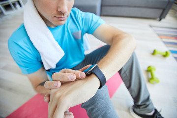 Fototapeta na wymiar Young active man checking time in smartwatch during break between trainings