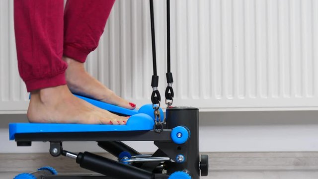 Woman doing exercises at home on stepping machine. Female legs foot on stepper trainer