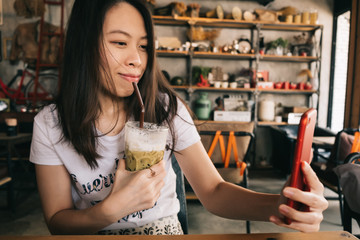 Young asian woman using smart phone camera for selfie in vintage cafe.